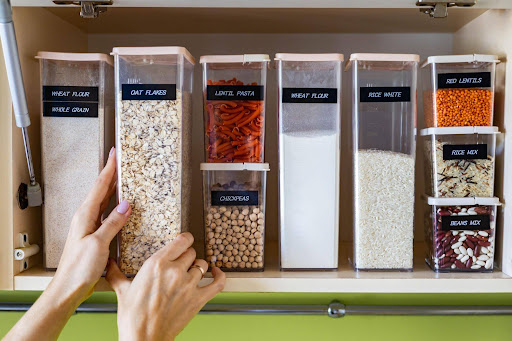 Labeled clear containers of grains, pasta, and legumes organized on a pantry shelf